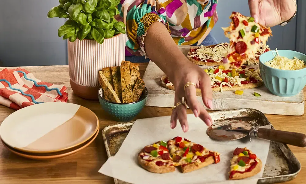 A person serving small low-carb pizzas and flatbreads at a kitchen table for Heylo.